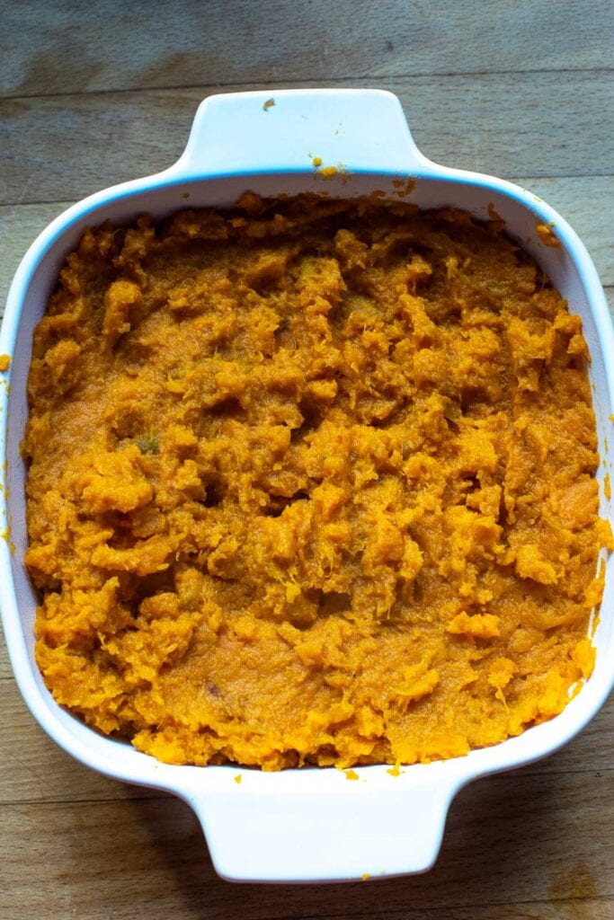 Mashed sweet potatoes in a casserole dish waiting to be topped with brown sugar and butter mixture before baking.