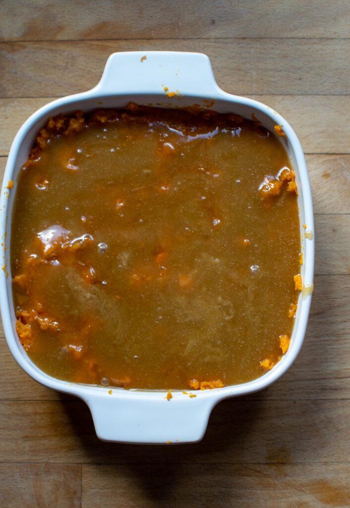 Caramelized brown sugar and butter mixture poured over top of mashed sweet potatoes in a casserole dish before baking.
