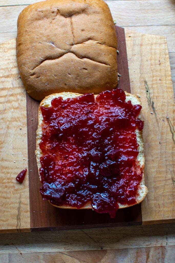 A square panini bun cut into a top and bottom and cranberry sauce spread to cover the bottom bun.