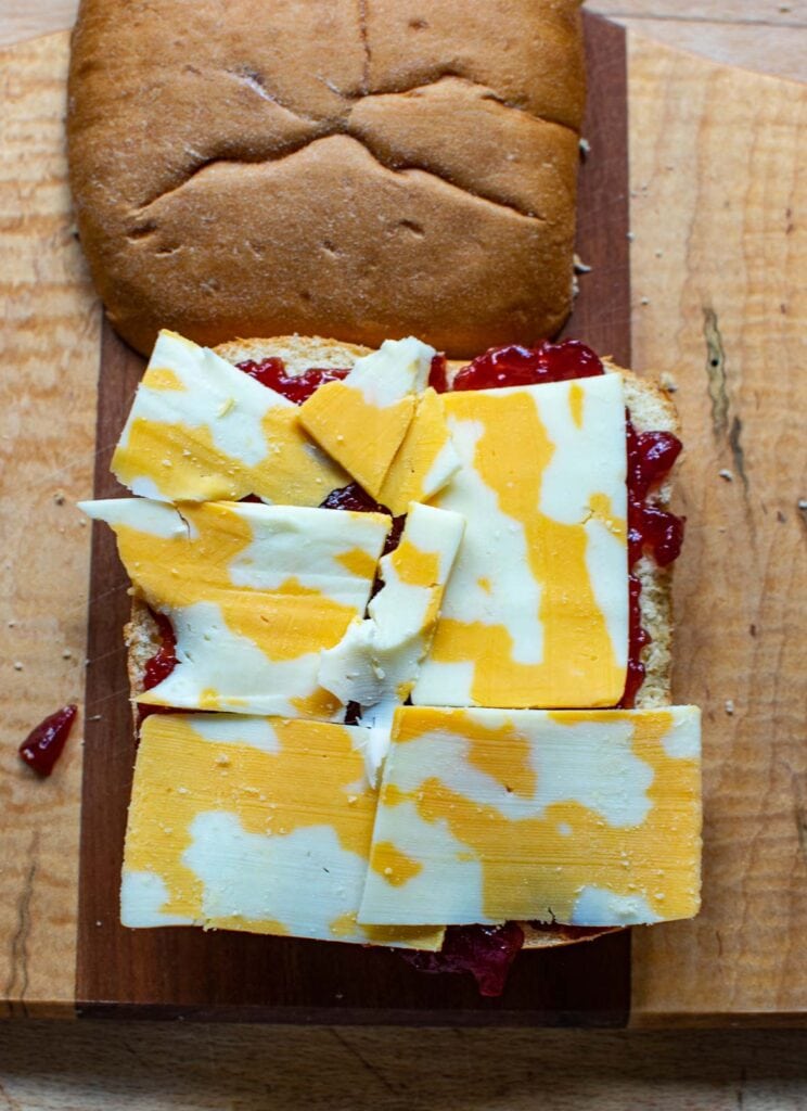 Marbled cheddar cheese slices on top of cranberry sauce spread on a panini bun half.