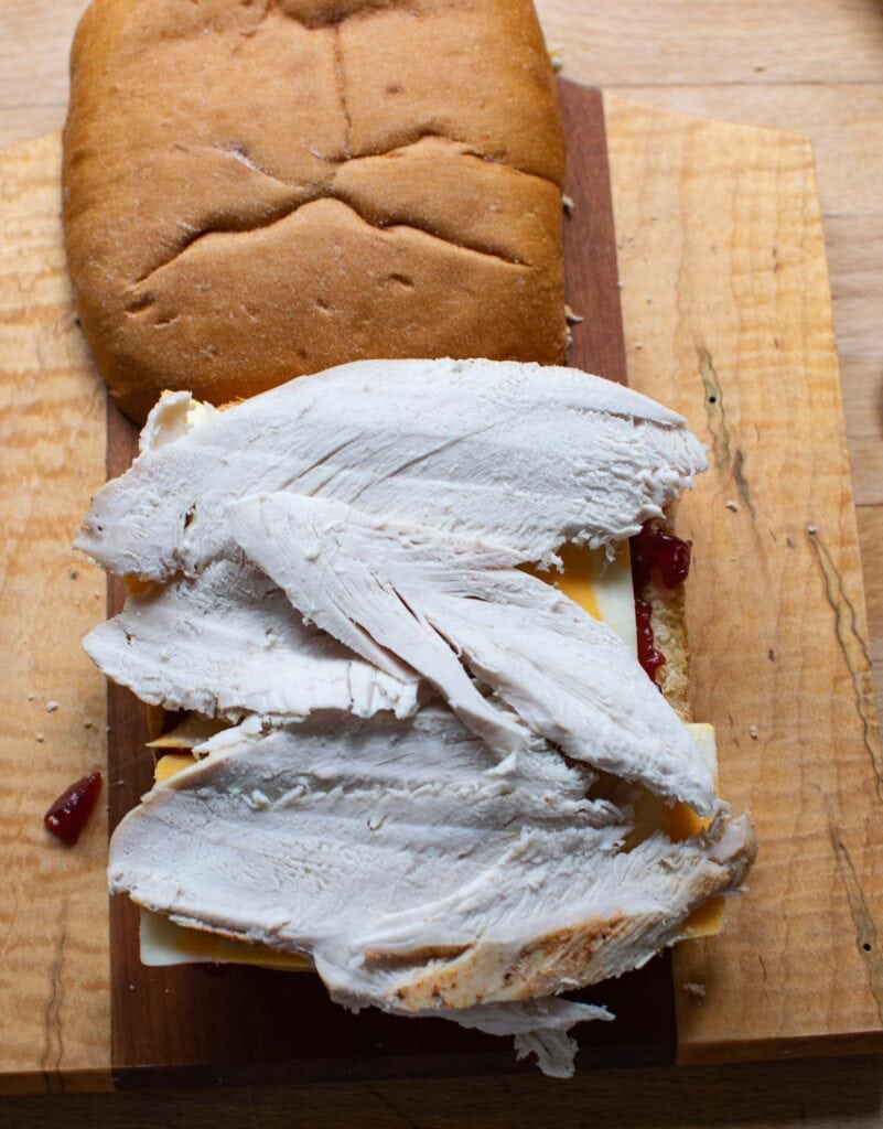 Sliced left over turkey  layered on cheese and cranberry sauce to make a leftover turkey sandwich.