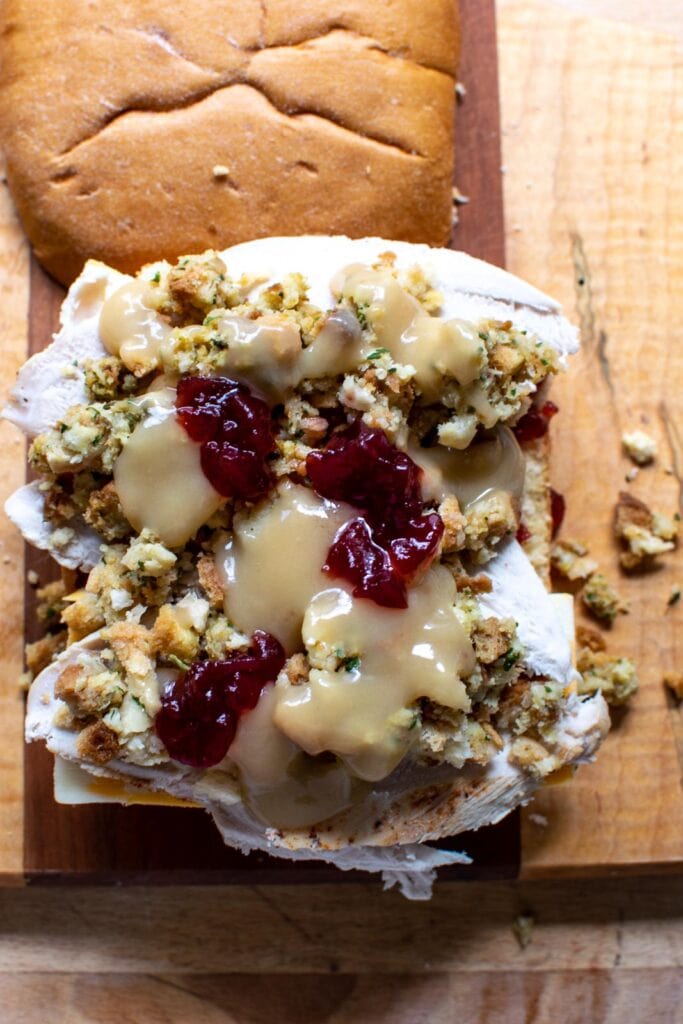 Cranberry sauce dolloped on top of layered of cheese, turkey, stuffing and gravy all on a panini bun.