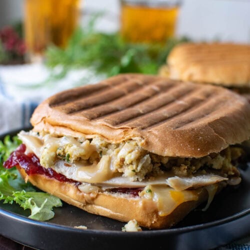 A sandwich made with leftover turkey, stuffing and cranberry sauce grilled and served on a plate with lettuce leaves for garnish.