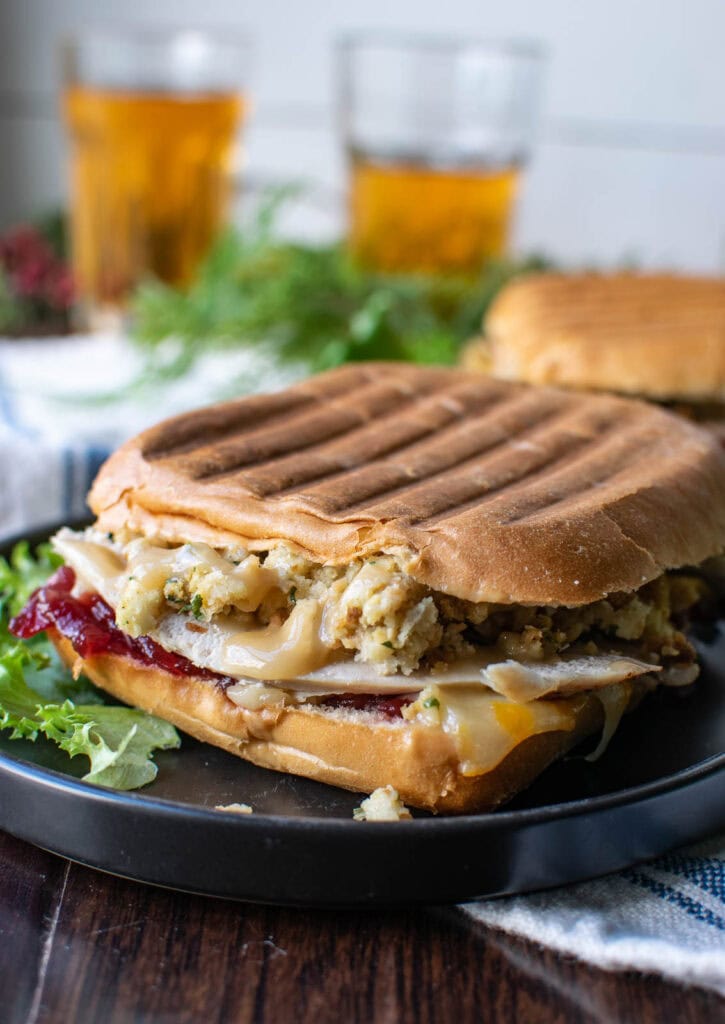 A sandwich made with leftover turkey, stuffing and cranberry sauce grilled and served on a plate with lettuce leaves for garnish.