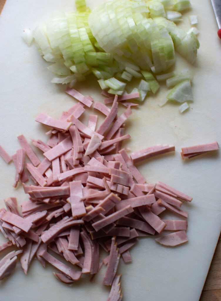 Chopped onions and sliced turkey bacon on a cutting board.