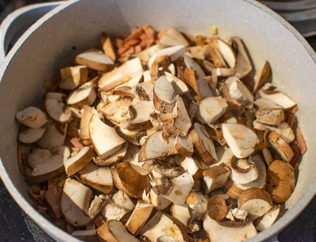 Sliced mushrooms that have been rough chopped and added to the frying pan with browned onion and bacon.
