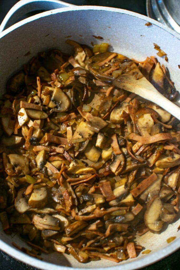 Mushrooms cooked down with onions and bacon in a large deep frying pan.