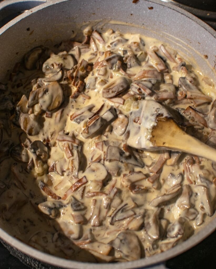 Creamy sauce with mushrooms, onions and sliced bacon in a deep, large frying pan.
