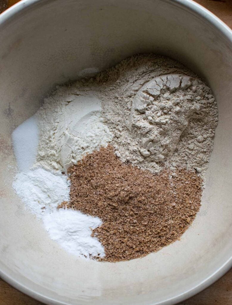 Flour, wheat bran, baking soda, baking powder and salt in a large ceramic mixing bowl before being mixed together.