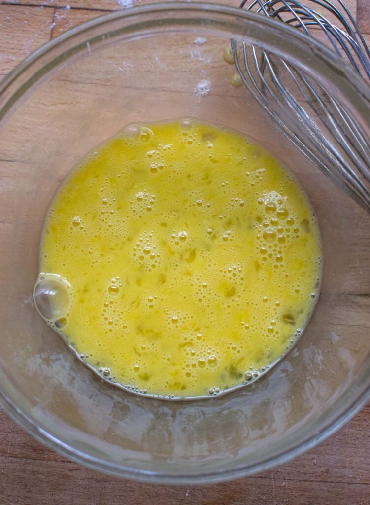 Two eggs beaten with a whisk in a glass mixing bowl.