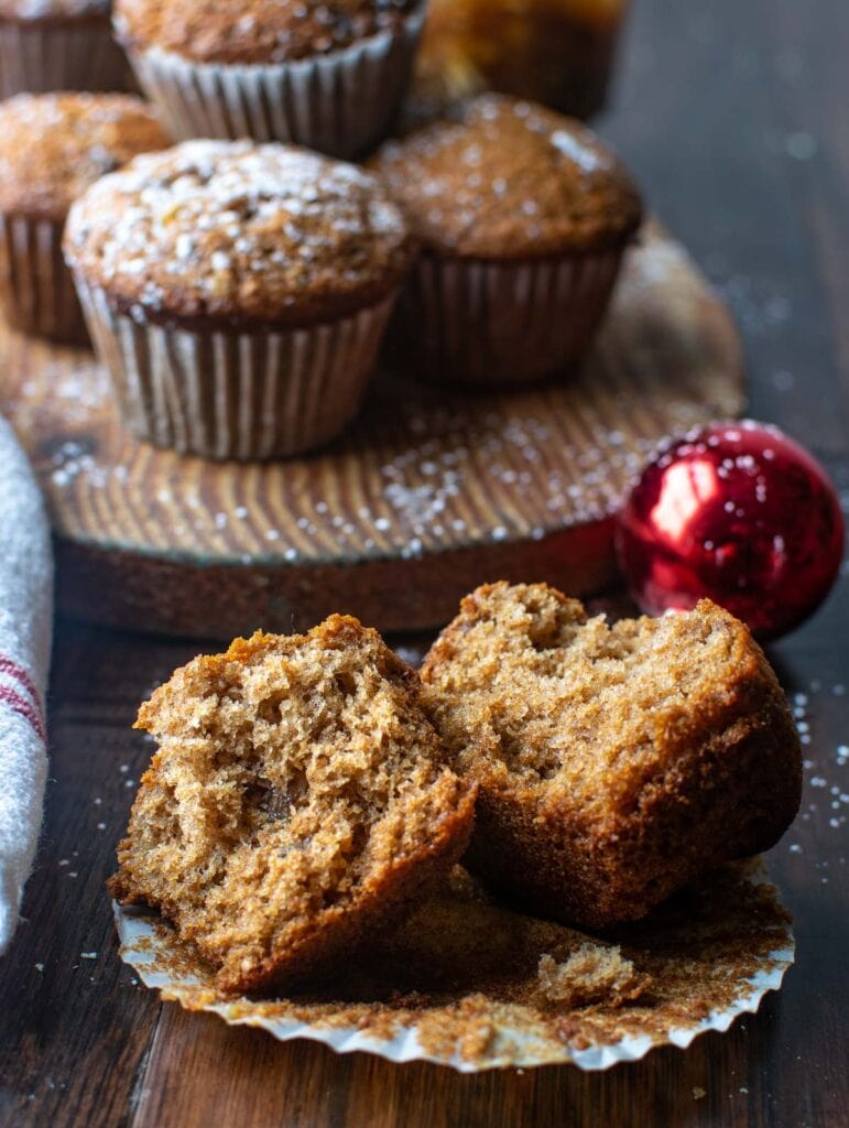 A mincemeat muffin torn in half to see the inside with a few muffins dusted with powdered sugar in the background.