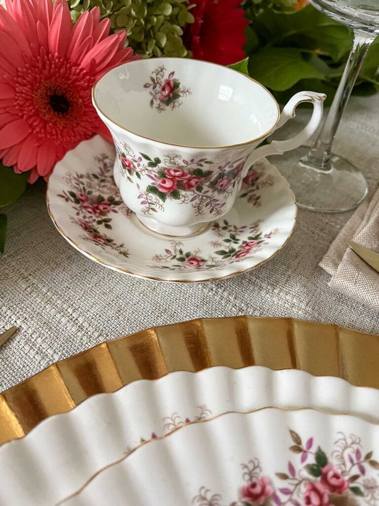 A teacup and saucer with pink roses are part of a place setting on a Thanksgiving table.