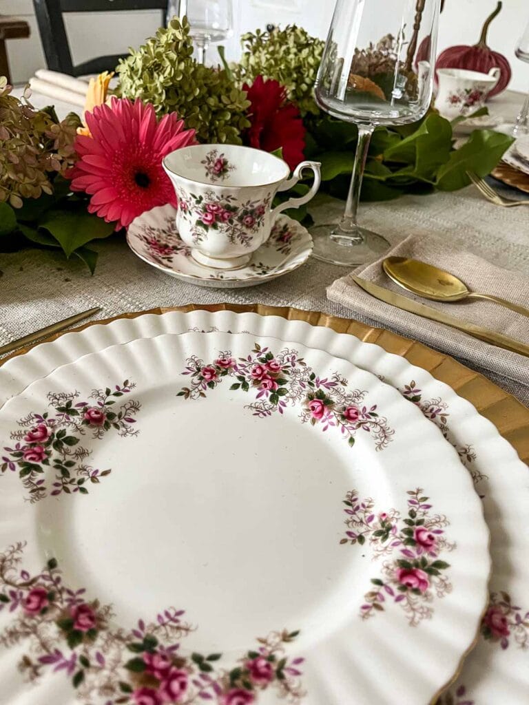A table set for Thanksgiving with Royal Albert Roses and Lavender dinnerware, gold flatware and a hydrangea centrepiece.