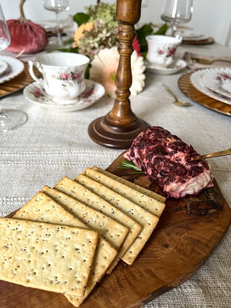 A wood board with a cranberry cheese log and crackers set on top.