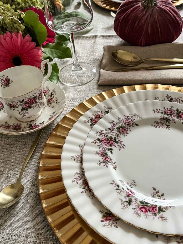 An elegant Thanksgiving table set with vintage china, with gold accents a fresh flower centrepiece.