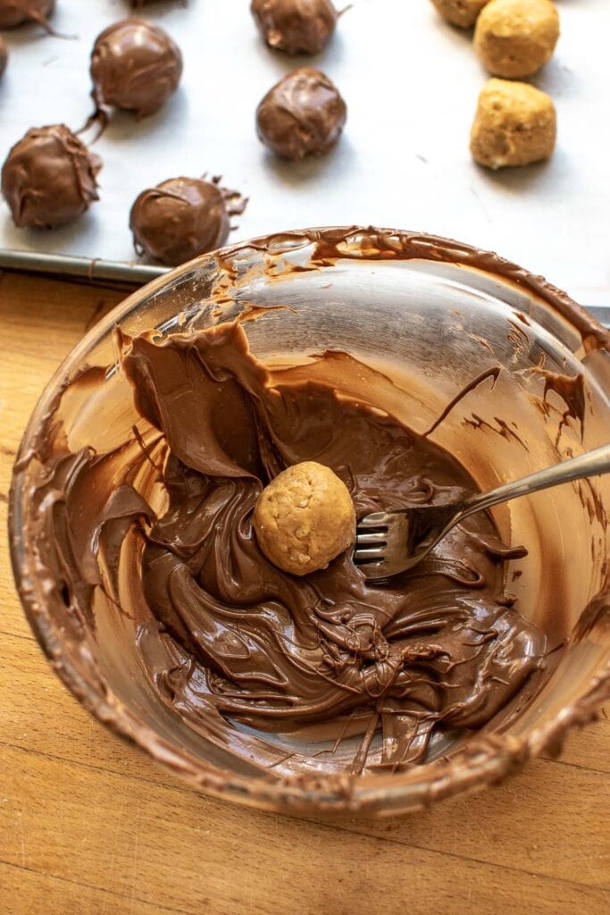 Peanut butter balls being dipping into melted chocolate with a fork.