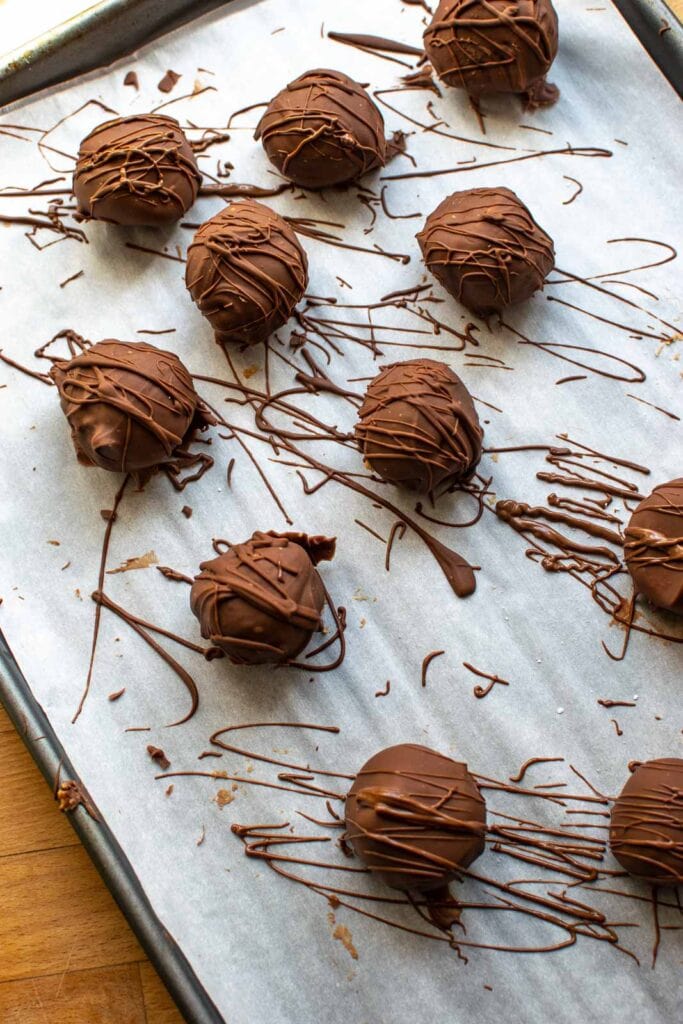 Chocolate coated Rice Krispie peanut butter balls on a parchment lined baking sheet and drizzled with more chocolate.