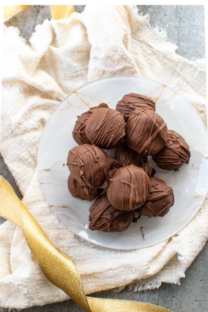 A plate of chocolate peanut butter balls on a gold and white marble plate sitting on top of a cream coloured napkin.