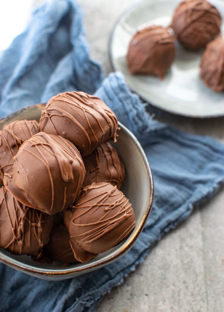 Chocolate covered Rice Krispie Peanut Butter balls in a small bowl sitting on top of a blue napkin.