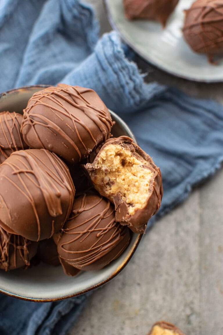 A bowl of chocolate covered Rice Krispie peanut butter balls on a blue gauze napkin.