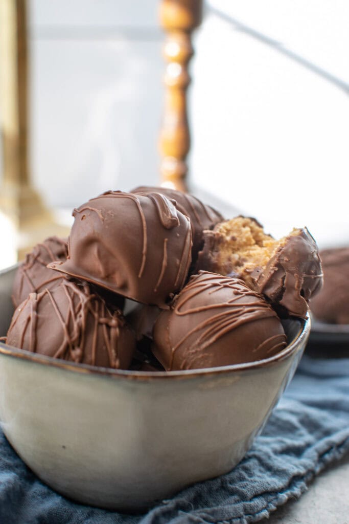 A bowl of chocolate peanut butter balls with a bite taken out of one of the balls.