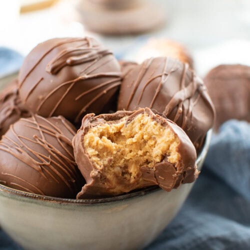 A bowl of chocolate covered peanut butter balls, one with a bite out of it exposing the peanut butter centre.