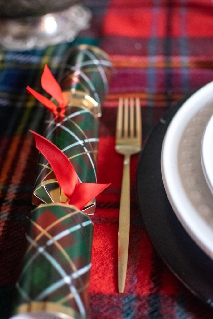 A tartan Christmas cracker beside a brushed gold dinner fork on a dinner table.