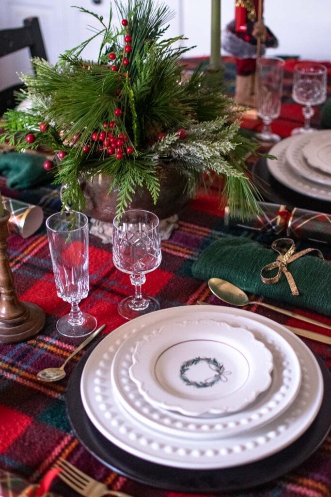 A Christmas tablescape with a tartan table cloth, green napkins and crystal glasses.