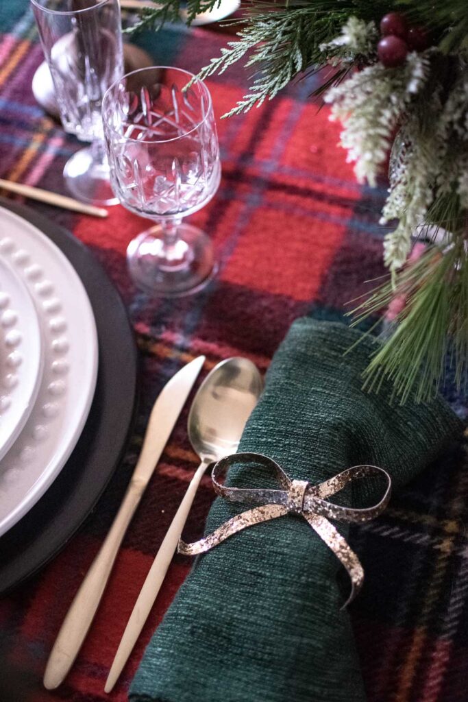 A Christmas dinner table set with crystal stemware, green linen napkins with a gold bow and crystal stemware.