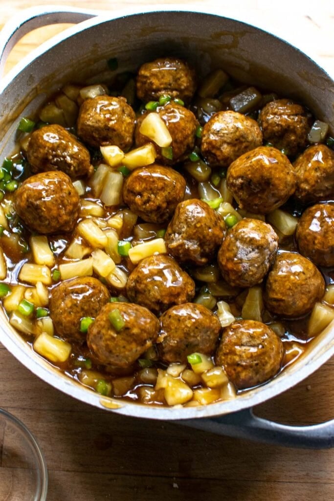 Meatballs stirred into sweet and sour sauce with pineapple and green pepper until full coated with sauce.