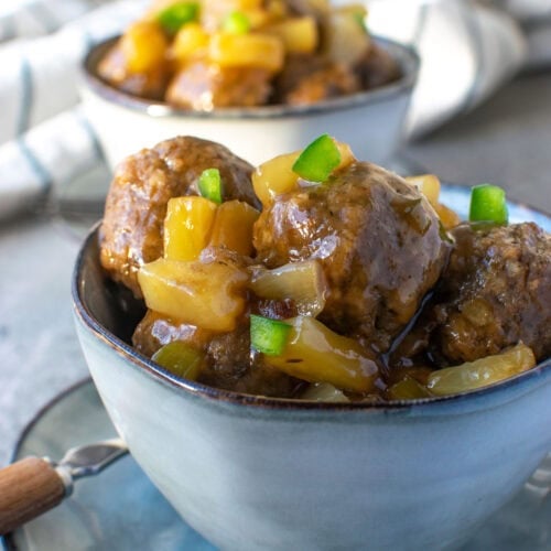 Two bowls of sweet and sour meatballs sitting on small plates and garnished with finely chopped green pepper.