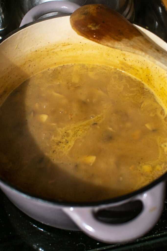 Cream of mushroom soup broth simmering in a soup pot on the stovetop.