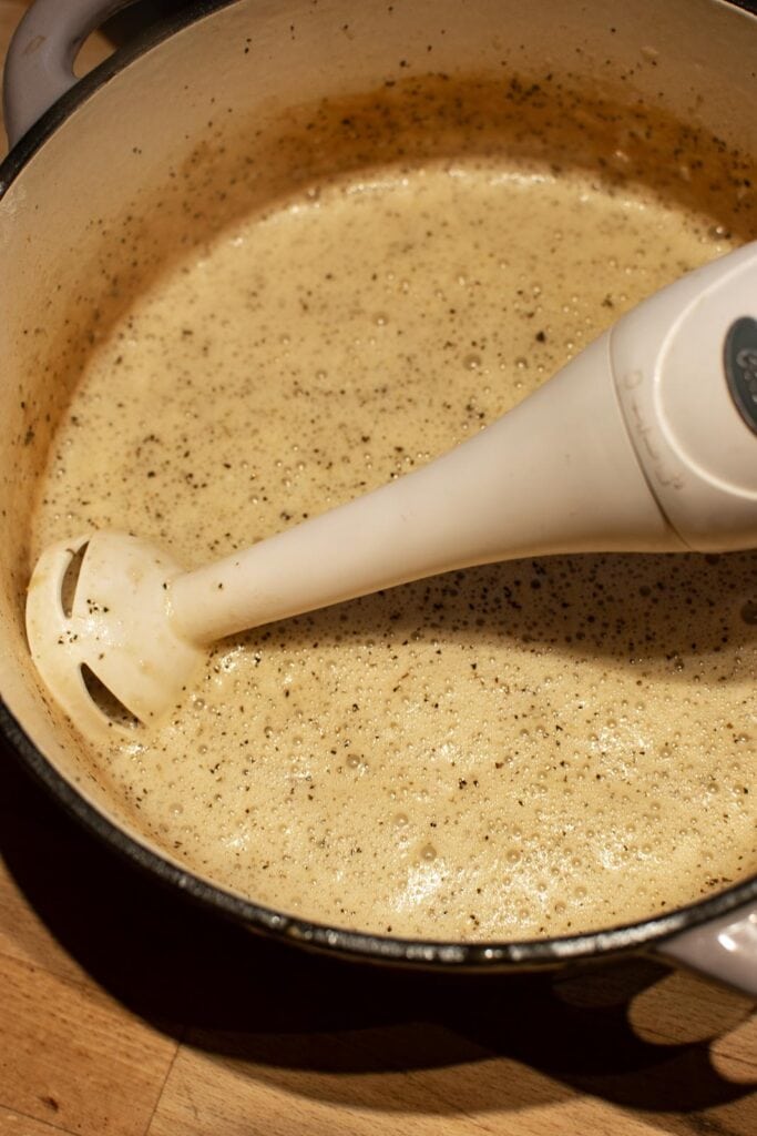 Light cream added to mushroom soup broth and processed to a creamy soup with a hand blender in pot.