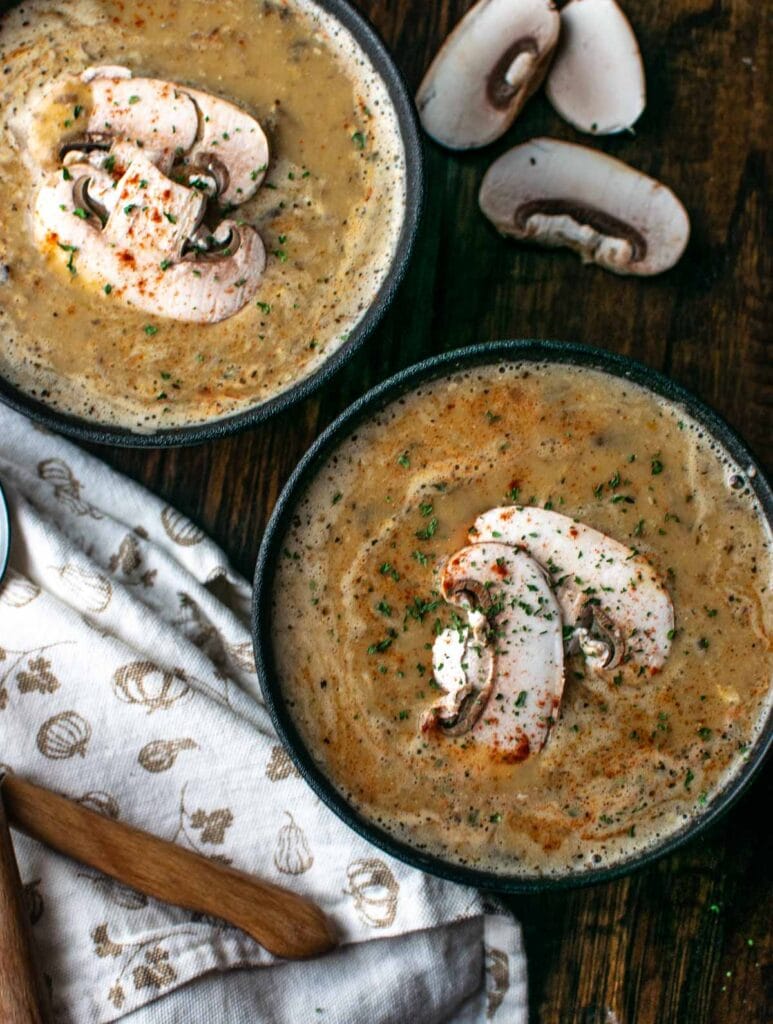 Two bowls of homemade cream of mushroom soup garnished with fresh mushrooms and paprika.