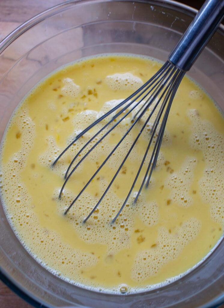 A mixture of eggs, milk and maple syrup whisked together in a mixing bowl.