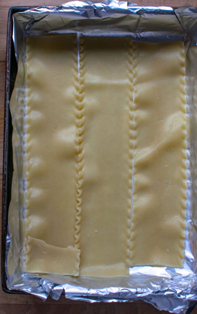 Cooked lasagna noodles lining the bottom of a 9 by 13 inch baking pan.