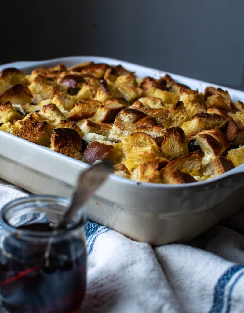 A freshly baked Blueberry French Toast Casserole with a jar of maple syrup in front of it.