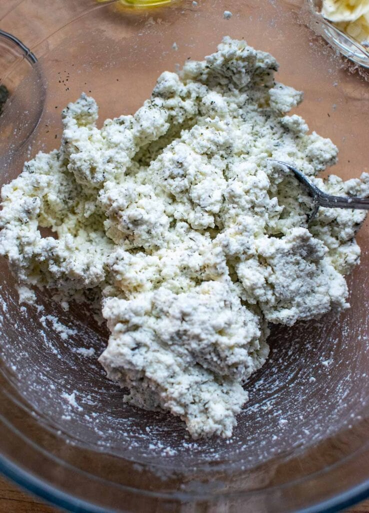Ricotta cheese mixed with dried dill, garlic powder and salt in a large glass mixing bowl.