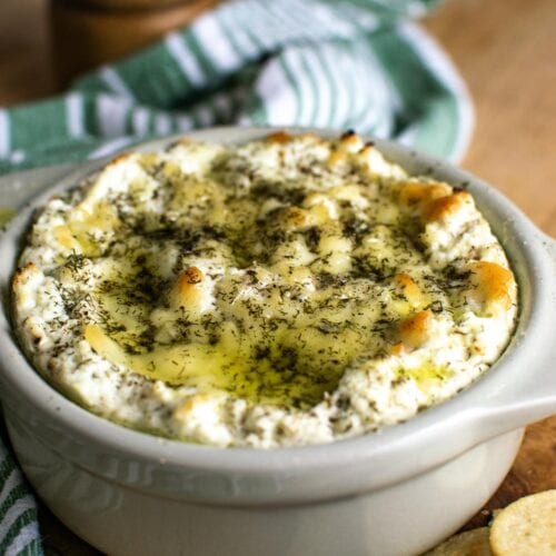 A ceramic baking dish with a baked cheese dip drizzled in olive oil.