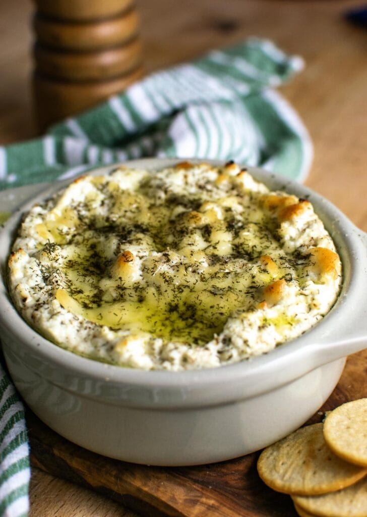A ceramic baking dish with a baked cheese dip drizzled in olive oil.