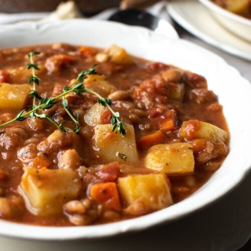 A bowl of potato and bean soup garnished with fresh thyme.