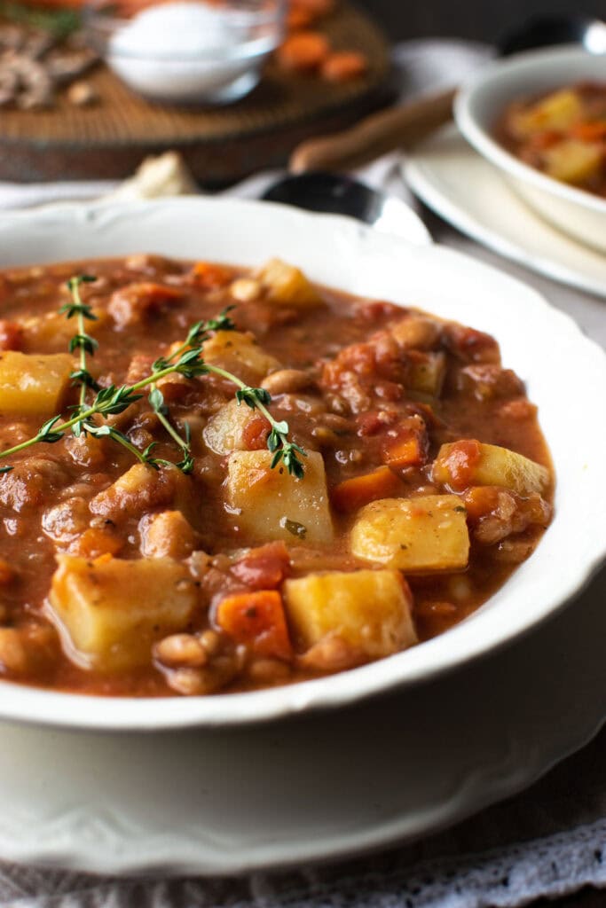 A bowl of potato and bean soup garnished with fresh thyme.