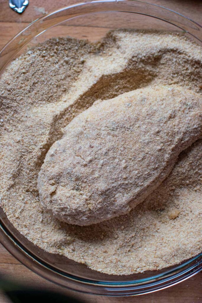 A mustard coated chicken breast fully coated with breadcrumbs before baking.