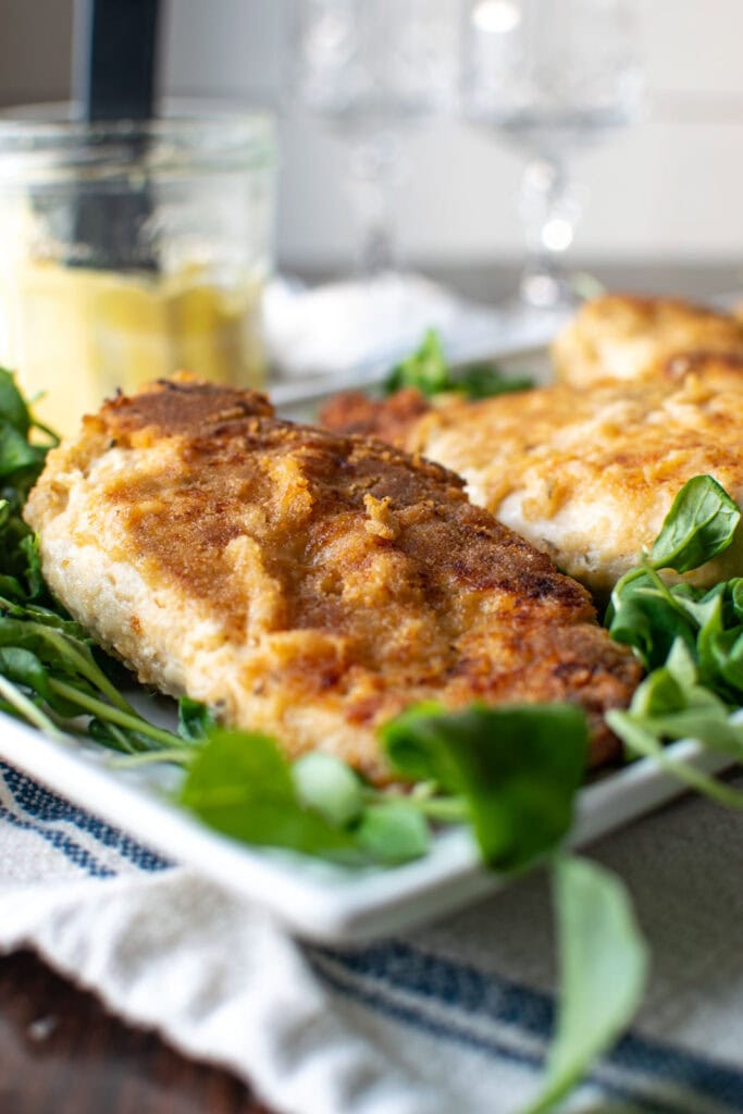 Crispy baked Dijon chicken breast after baking, served on a platter of baby spinach.