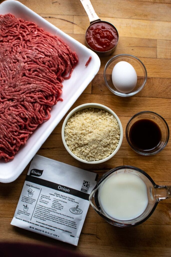 Ingredients to make glazed meatloaf including hamburger, egg, breadcrumbs, milk, onion soup mix and Worcestershire sauce.