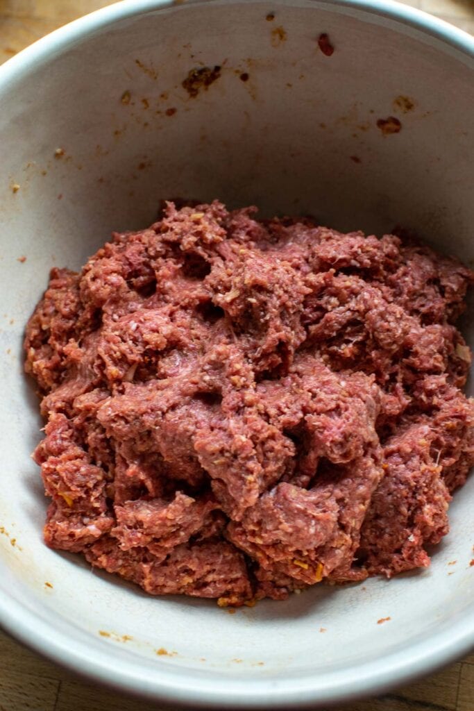 A large mixing bowl with ground beef mixed with bread crumbs, onion soup mix, tomato sauce and other ingredients to make meatloaf.