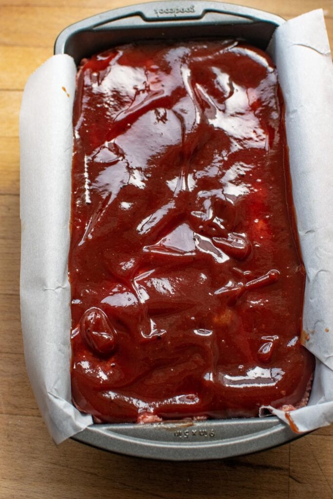 Glazed meatloaf in a parchment lined loaf pan before baking.