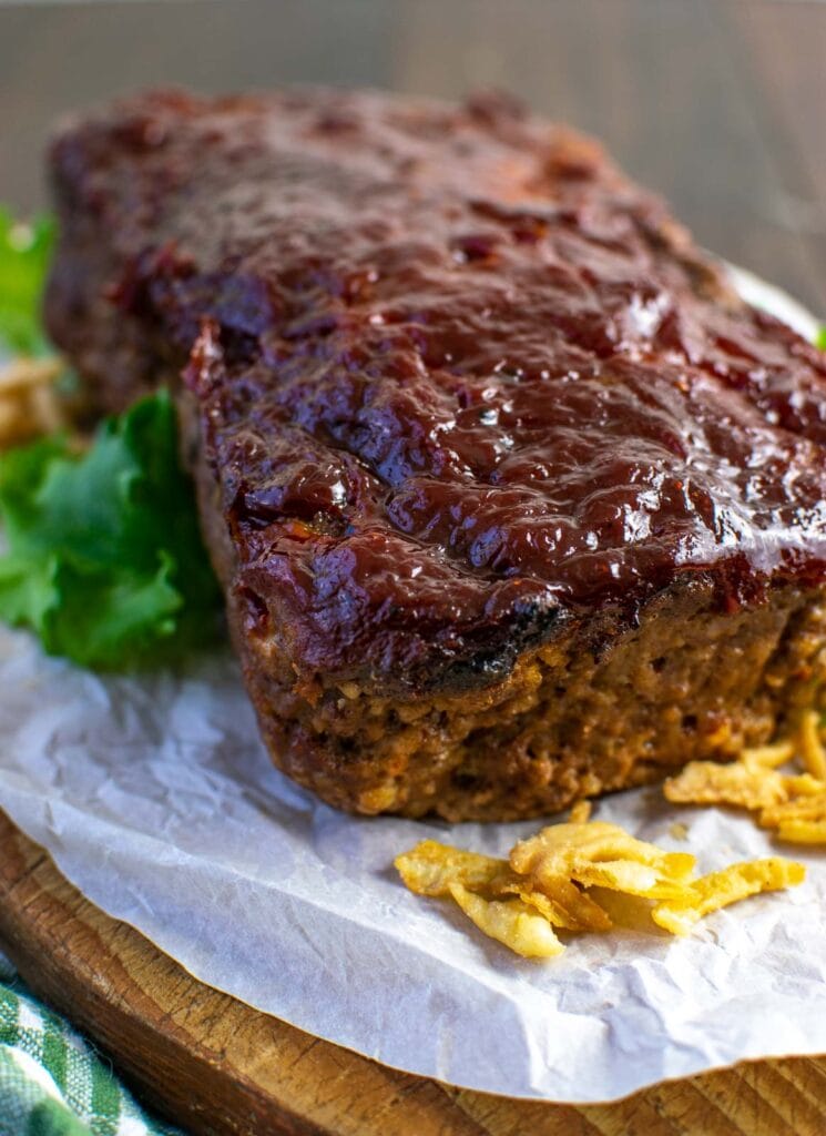 A meatloaf glazed with a ketchup sauce on a parchment lined wood cutting board, and crispy fried onions around it.