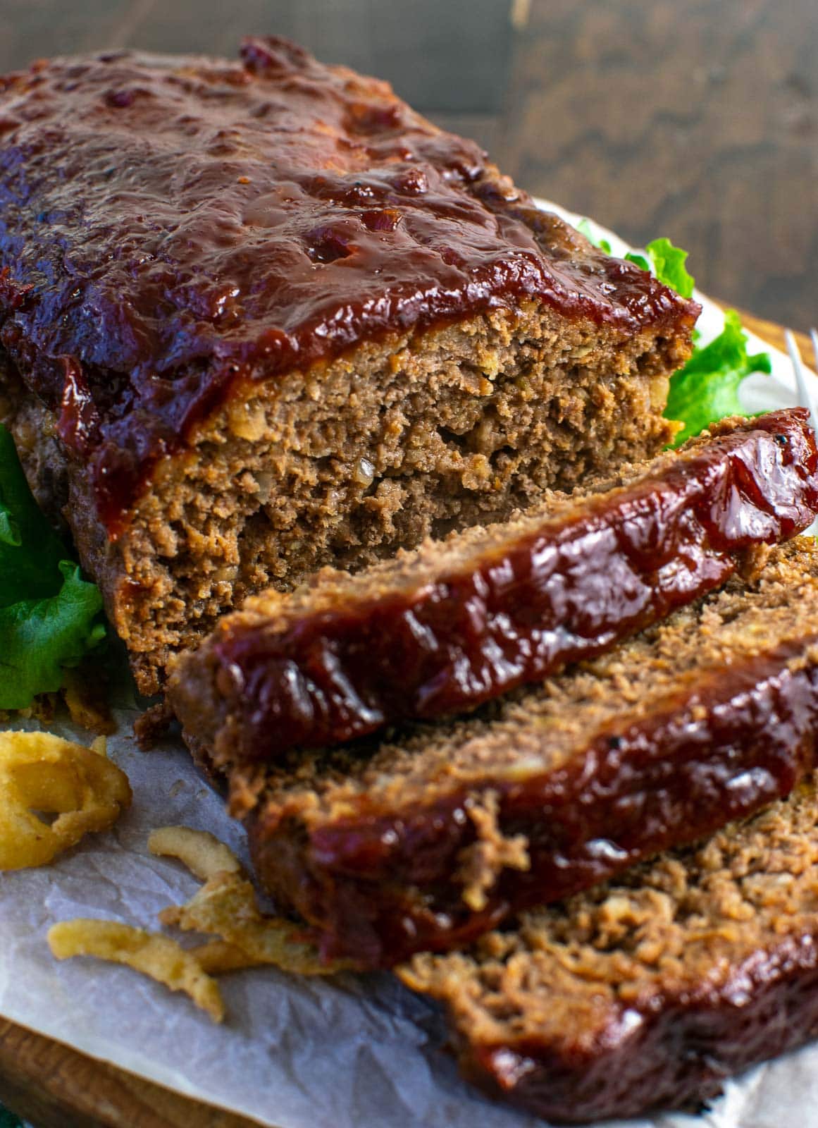 Glazed meatloaf on a parchment lined cutting board with 3 slices cut to fall from the end of the loaf.