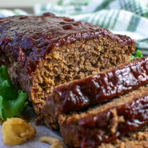 A meatloaf glazed on a wood platter with a few slices cut away from the end.